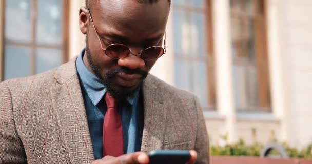 Bir bankta oturan ve akıllı telefonundan yazarak genç Afrikalı-Amerikalı adam. İş ve yaşam tarzı kavramları — Stok video