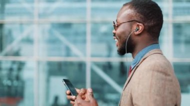 Afrika kökenli Amerikalı işadamı Ofis Binası yakınındaki kulaklık ile telefonda konuşurken güneş gözlüğü. İş, insanlar, müzik, teknoloji, eğlence ve yaşam tarzı kavramı
