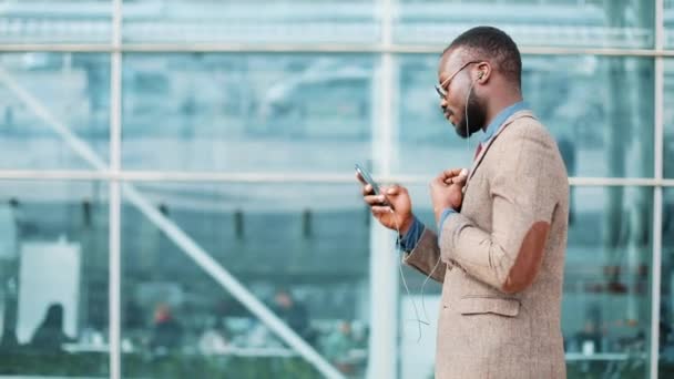 Afro-amerikai üzletember, a napszemüveg, beszél a telefonon, a fejhallgató a hivatali épület közelében. Üzleti, ember, zene, technológia, szabadidős és életmód fogalma — Stock videók