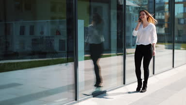 Office center yakınındaki sokakta yürürken smartphone üzerinde konuşmak mutlu genç kız. Kadın iş kıyafetleri yaz zamanında giyinmiş. İletişim ve başarılı iş kavramı