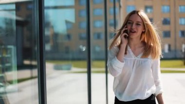 Office center yakınındaki sokakta yürürken smartphone üzerinde konuşmak mutlu genç kız. Kadın iş kıyafetleri yaz zamanında giyinmiş. İletişim ve başarılı iş kavramı