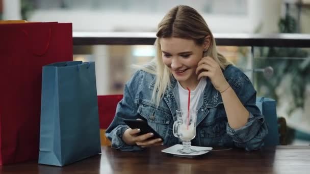 女孩检查她的手机坐在咖啡馆的购物袋 — 图库视频影像