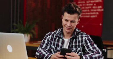 Genç sohbet, yazarak ve masada otururken Smartphone cep telefonu ile kentsel güzel ofiste yazarak işadamı gülümsüyor. Kapalı, ağır çekim. İletişim, başarılı iş kavramı