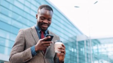 Mutlu Afrika kökenli Amerikalı adam bir şey office center yanında ayakta dışında onun smartphone içinde türleri. İletişim, mobil teknoloji, yaşam tarzları ve başarılı iş kavramı