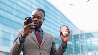 Mutlu Afro-Amerikan başarılı iş adamı smartphone üzerinde harika bir haber alır. Bir office center yanında duruyor. Akıllı telefon app kavramı