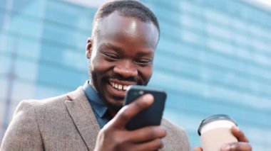 Mutlu Afro-Amerikan başarılı iş adamı smartphone üzerinde harika bir haber alır. Bir office center yanında duruyor. Akıllı telefon app kavramı