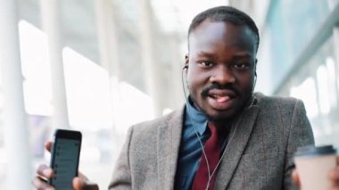 Ofis ve komik ritmine dans dışında yürüyüş smartphone, kulaklıktan müzik dinlerken mutlu Afrika kökenli Amerikalı iş adamı. Komik dans hamle kahve. Yakın çekim, yavaş hareket