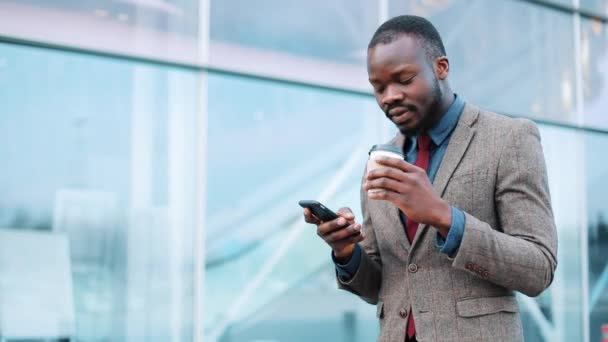 Junge afrikanisch-amerikanische Mann mit App auf dem Smartphone in der Stadt in der Nähe des Bürozentrums schöner junger Geschäftsmann mit Smartphone lächelt glücklich. — Stockvideo