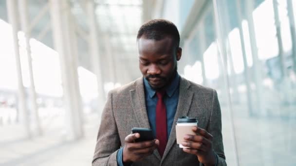 Африканський Americanman Янг за допомогою app на смартфон в місті поблизу офіс центр красивий Молодий підприємець за допомогою смартфона посміхаючись щасливі. — стокове відео