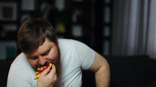 Hombre con sobrepeso débil comiendo pizza y bebiendo cerveza sentado en el sofá. Concepto de desnutrición, deporte, obesidad — Vídeo de stock
