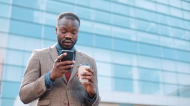 Yorgun ve stresli bir Afrikalı-Amerikalı işadamı bir şey ayakta dışında onun smartphone içinde okur. Adam sms manifatura app City akıllı telefon kullanma.