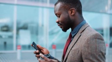 Yorgun ve stresli bir Afrikalı-Amerikalı işadamı office center yakınındaki sokakta yürürken bir akıllı telefon kullanır. Başarısız olan iş, iflas, stok artış kavramı