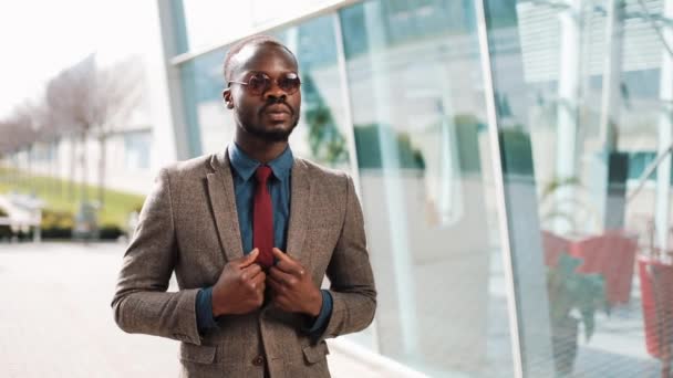 Bonito empresário afro-americano à espera de uma mensagem no seu smartphone. Homem negro ao pé do prédio de escritórios. Conceito de negócios, pessoas, comunicação, tecnologia, lazer e estilo de vida — Vídeo de Stock