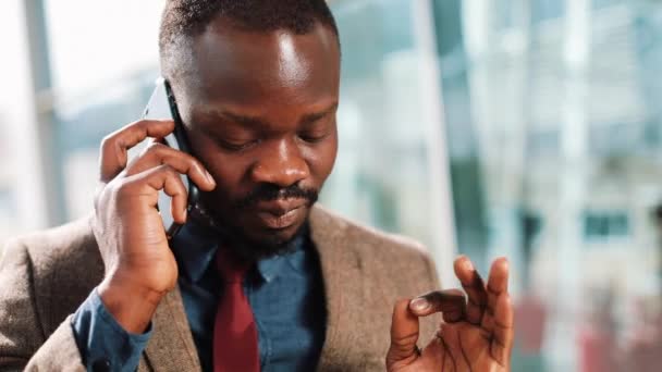 Empresário afro-americano conversa com alguém em seu smartphone em pé na rua perto do centro de escritórios. Conceito de negócios, pessoas, comunicação, tecnologia, lazer e estilo de vida . — Vídeo de Stock