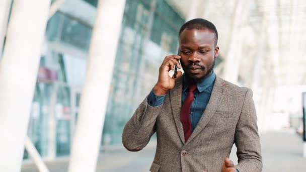 Uomo d'affari afroamericano che cammina per strada vicino al centro degli uffici e parla al cellulare. Business, persone, comunicazione, tecnologia, tempo libero e stile di vita — Video Stock