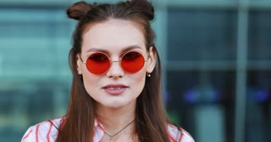 Kırmızı güneş gözlüğü moda güzel fotoğraf makinesi ile modern cam bina önce teşkil etmektedir. Kameraya bakarak bir genç transseksüel