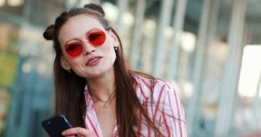 Kırmızı güneş gözlüğü moda güzel fotoğraf makinesi ile modern cam bina önce teşkil etmektedir. Kameraya bakarak bir genç transseksüel