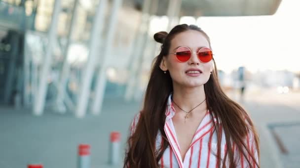 Modemodel mit roter Sonnenbrille läuft selbstbewusst die Straße in der Nähe des Einkaufszentrums entlang. Sommerzeit — Stockvideo