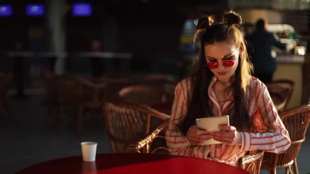 Mujer joven lee algo en sus mesas sentado a la mesa en la cafetería afuera — Vídeos de Stock