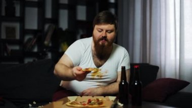 Sakallı şişman adam bira ile masada oturan ve Mısır-televizyon önce pizza yiyor