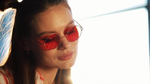Mujer atractiva joven en gafas de sol rojas usando tableta con pantalla táctil en un café. Hermosa chica en el aeropuerto o centro comercial con la tableta — Vídeo de stock