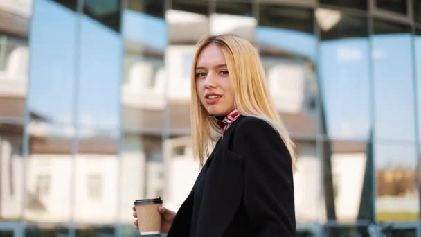 Jeune femme transgenre marche avec une tasse de café le long du mur miroir à l'extérieur — Video