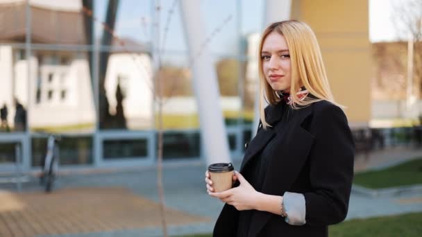 Hübsche junge blonde Frau steht mit einer Tasse Kaffee vor einer Spiegelwand draußen — Stockvideo