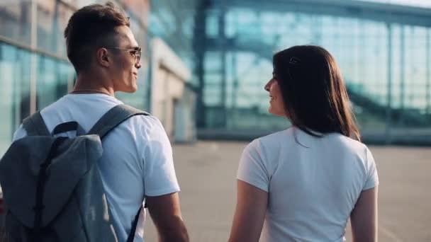 Jovem casal feliz vai com bagagem perto do aeroporto ou da estação ferroviária. O conceito de viagem, férias, feriados. Hora de verão, pôr do sol — Vídeo de Stock