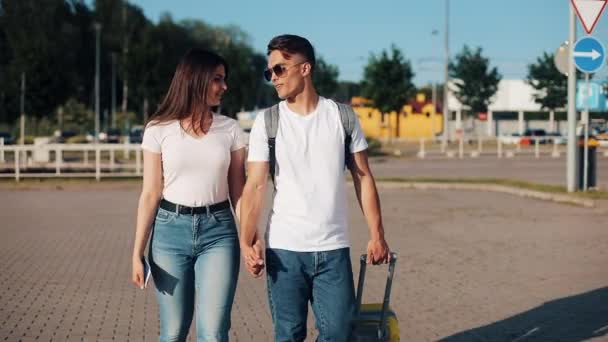Happy young couple goes with luggage near the airport or railway station. The concept of travel, vacations, holidays. Summer time, sunset — Stock Video