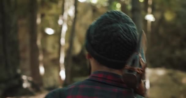 Walking bearded lumberjack with axe. Man in a cap walks through the woods in search of the tree. View behind the back — Stock Video