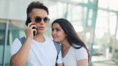 Çekici genç çift ayakta Havaalanı yakınında. Bir adam bir taksi veya teslimat servisi çağırır. İletişim, teknoloji, smartphone kavramı