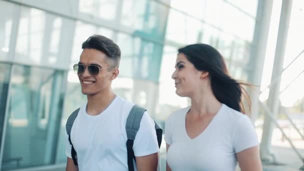 Jovem casal feliz vai com bagagem perto do aeroporto ou da estação ferroviária. O conceito de viagem, férias, feriados. Hora de verão, pôr-do-sol. Movimento lento — Vídeo de Stock