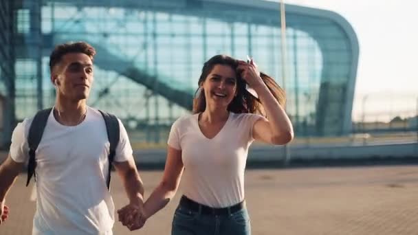 Pareja joven y feliz con mochilas y pasaportes en sus manos corren al aeropuerto o estación de tren. El concepto de viajes, vacaciones, vacaciones. Hora de verano, puesta de sol — Vídeo de stock