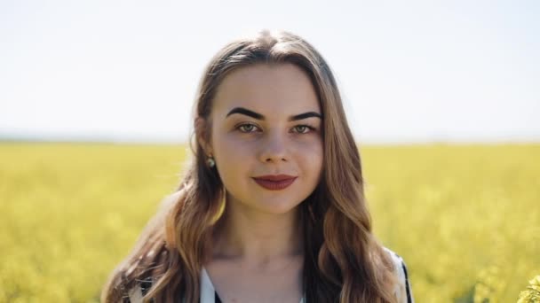 Menina bonita retrato olhando para a câmera no campo de estupro. Jovem mulher de pé no campo de estupros, posando, e sorrindo para a câmera — Vídeo de Stock