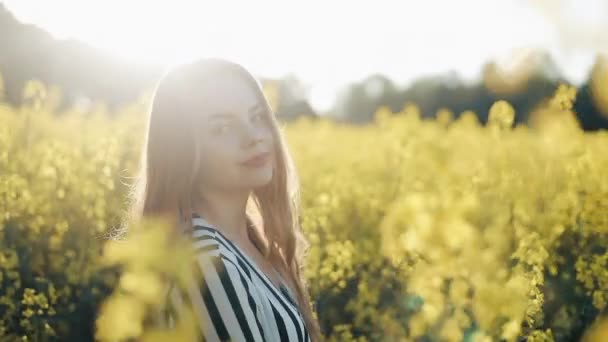 Hübsches Mädchen geht auf das Vergewaltigungsfeld, posiert und lächelt in die Kamera. schöne junge Frau auf dem Feld der Rapssamen gelbe Blumen, sonniger Tag — Stockvideo