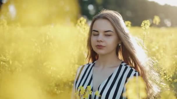 Portret Ładna dziewczyna patrząc na kamery w polu rzepaku. Młoda kobieta idzie w polu gwałty, pozowanie i uśmiecha się do kamery — Wideo stockowe