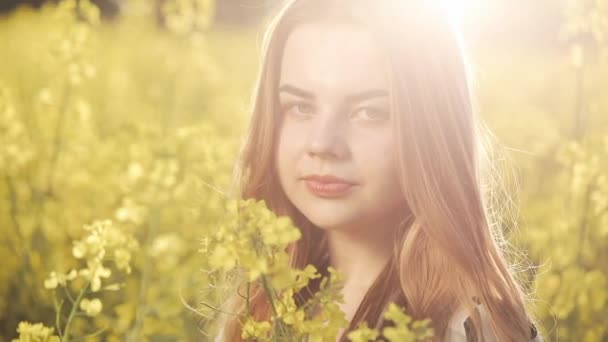 Menina bonita retrato olhando para a câmera no campo de estupro. Jovem caminha no campo de estupros, posando e sorrindo para a câmera — Vídeo de Stock