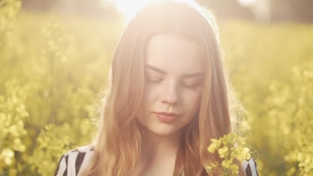 美丽的年轻女孩在油菜籽黄色的花朵, 阳光明媚的一天 — 图库视频影像