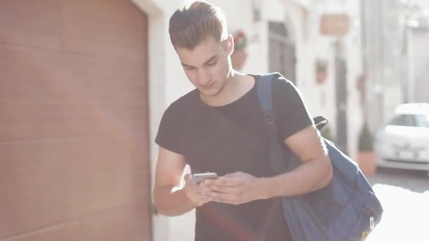A portrait of a handsome young man surfing smartphone and walking about the town. Sunny background. Blurred background — Stock Video