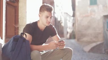 Giriş merdiven oturan ve cep telefonuyla sırt çantası ile genç Turizm