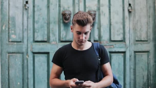 Retrato de jovem bonito usando celular na cidade velha. Movimento lento — Vídeo de Stock