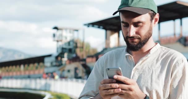 Hästkapplöpning. Man satsa på en häst med en smartphone. Ung man använder en smartphone på en travbana. Den bookmaker vinner — Stockvideo