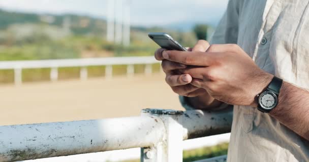 Ιπποδρομίες. Ο άνθρωπος που στοιχηματίζετε σε ένα άλογο με ένα smartphone. Νεαρός άνδρας χρησιμοποιεί ένα smartphone σε μια πίστα. Τα κέρδη στοιχημάτων — Αρχείο Βίντεο
