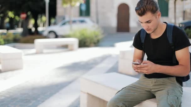 Vonzó fiatal ember, egy hátizsákban telefont ül a régi város technológia elfoglalt portré közelről modern jóképű smartphone ambiciózus mobil naplemente lassú mozgás — Stock videók