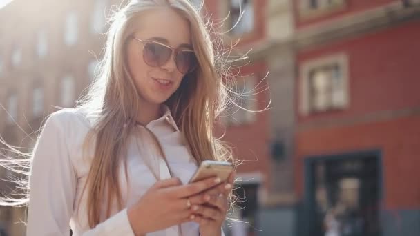 Beautiful young business woman wearing white shirt and using smartphone while walking in the city center summer internet business outside technology eye spring mobile slow motion street happy — Stock Video