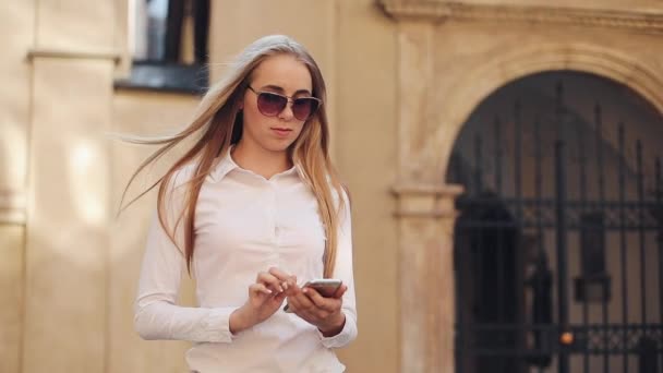 Hermosa mujer de negocios joven con camisa blanca y el uso de teléfono inteligente mientras camina en el centro de la ciudad negocio de Internet de verano fuera de la tecnología ojo primavera móvil cámara lenta calle feliz — Vídeo de stock