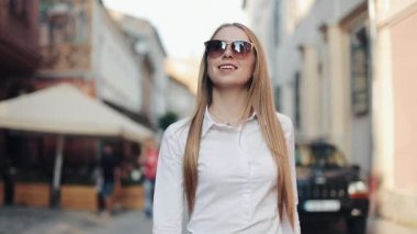 Çok gülümseyen genç kadın şık bir görünüm içinde güvenle güneş gözlüğü takıyor sokakta yürüyor. Hayat, aktif yaşam tarzı, moda blogger, podyum sevinci