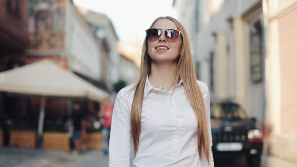 Çok gülümseyen genç kadın şık bir görünüm içinde güvenle güneş gözlüğü takıyor sokakta yürüyor. Hayat, aktif yaşam tarzı, moda blogger, podyum sevinci — Stok video