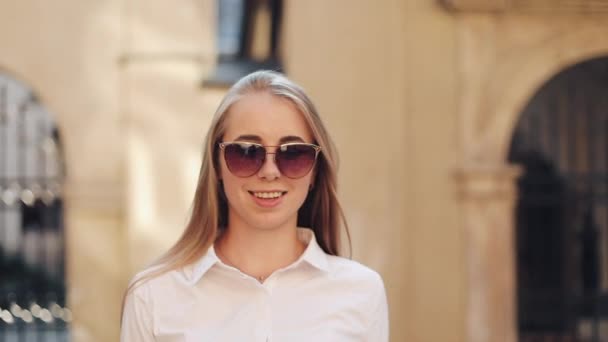Çok gülümseyen genç kadın şık bir görünüm içinde güvenle güneş gözlüğü takıyor sokakta yürüyor, saç parlak güneş ışığı dokunur. Hayat, aktif yaşam tarzı, moda blogger, podyum sevinci — Stok video