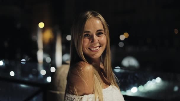 Atraktivní šťastná dívka při pohledu do kamery. Portrét krásné mladé ženy v noci ve městě, zpomalené. noční rozmazané pozadí — Stock video